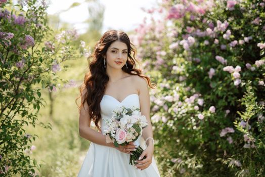 young girl bride in a white dress in a spring forest in lilac bushes on a wedding day