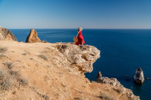 A woman in a red flying dress fluttering in the wind, against the backdrop of the sea