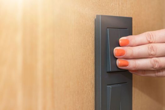 Turn on the light, a woman's hand presses the switch in the apartment close-up. Black light switch on the background of a wooden wall. The concept of saving electricity, the cost of electricity