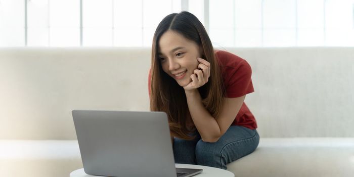 An attractive young woman is working on a laptop while sitting on sofa at home.