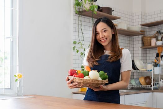 Portrait of Asian young woman look at camera. Attractive beautiful woman wear apron in cozy kitchen with fresh organic vegetables on table cooking healthy vegetable salad, healthy food active life.