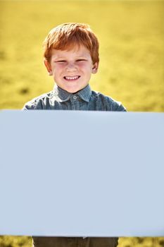 This is some exciting news. Portrait of a little boy holding a blank board outdoors