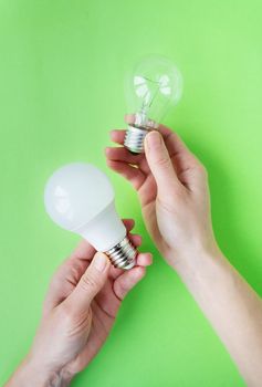 A set of two types of lamps, LED and incandescent, in the hands of a girl isolated on a green background. Energy-saving lamps