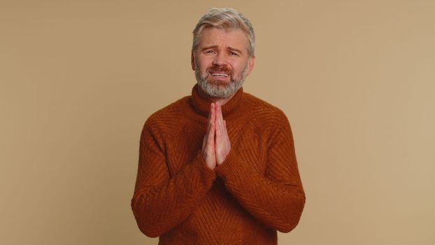 Please, God help, forgive me. Middle-aged old man praying, looking upward and making wish, asking with hopeful imploring expression, begging apology. Senior mature guy on beige studio background