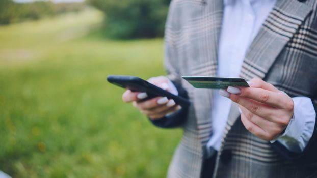 A young business lady makes a purchase with her phone and bank card in the park