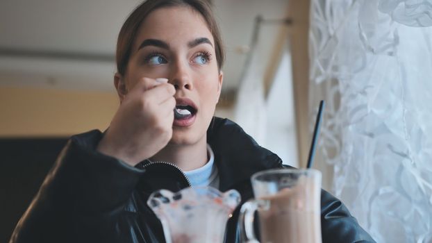 A girl is eating ice cream in front of a cappuccino in a coffee shop