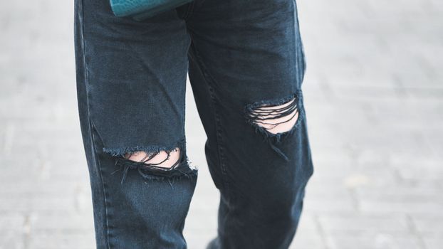 A girl in torn jeans walks through the city