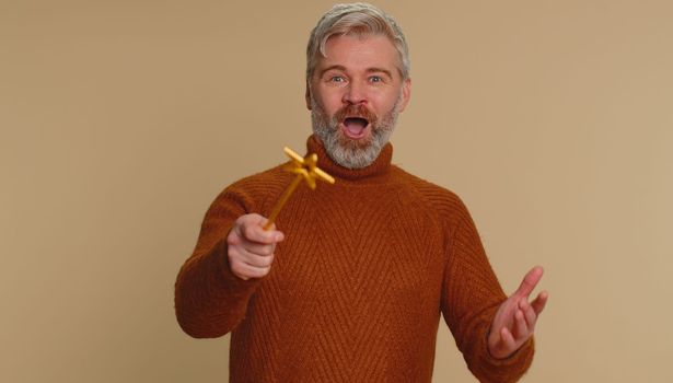 Magician witch man gesturing with magic wand fairy stick, making wish come true, casting magician spell, advertising holidays sale discount. Senior middle-aged guy isolated on beige studio background