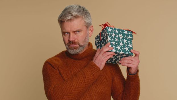 Happy middle-aged man opening gift box, unwrapping birthday surprise and expressing great happiness amazement, satisfied with best present bonus. Senior mature guy isolated on beige studio background