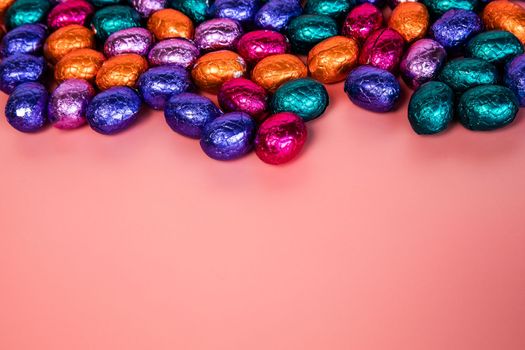 Pile of shiny wrapped chocolate Easter eggs, in colors red, blue and golden,green and purple. Festive Easter concept, top view pink background Happy easter close-up candy sweets concept stack