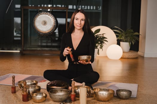 A woman in the lotus position using a singing bowl indoors . Relaxation and meditation. Sound therapy, alternative medicine. Buddhist healing practices.