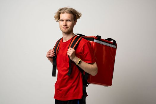 Smiling courier delivery man with a curly hair in red uniform with thermo bag isolated on white background. Delivery service