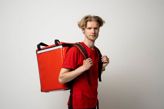 Young courier delivery man in red uniform with thermo bag isolated on white background. Delivery service