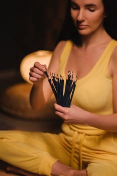 A girl in yellow clothes sitting on the floor holding pencils for drawing.