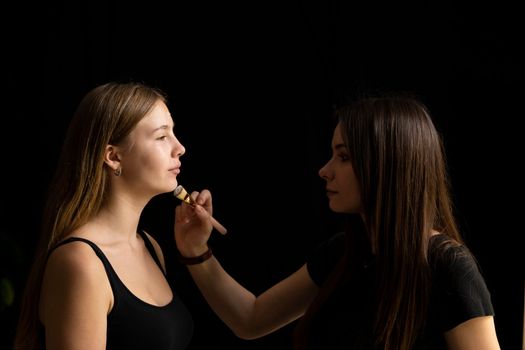 Make-up artist working with brush on model face. Portrait of young blonde woman in beauty salon interior. Process of making makeup. Applying toner to skin