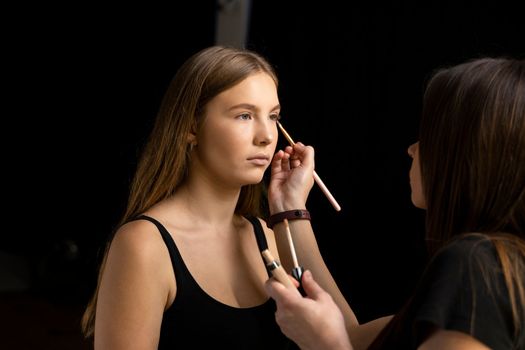 A beautiful young woman with long hair doing makeup for a wedding or photo shoot. Work of a make-up artist. The morning of the bride. Decorative cosmetics