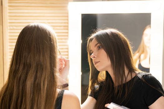 Make-up artist working with brush on model face. Portrait of young blonde woman in beauty salon interior. Process of making makeup. Applying toner to skin