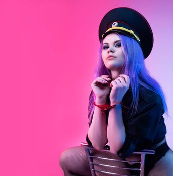 Sexy girl in police uniform for sexual games with handcuffs in neon light on the light background