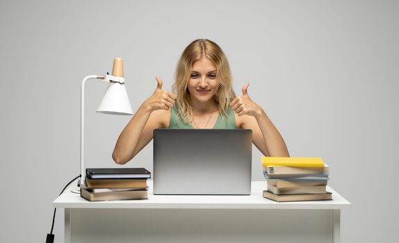 Cheerful office worker business student woman freelancer showing two thumbs up in front of laptop while speaking with a partners or clients