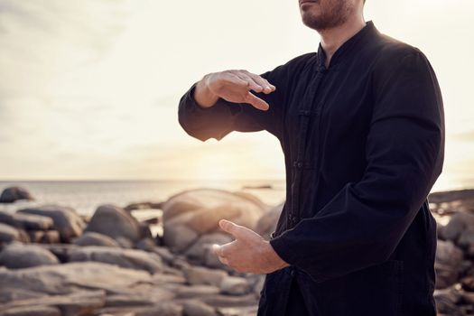 Beach, peace and tai chi, man in nature for balance and peace for mental wellness or control of body and mind. Spiritual health, fitness and meditation, energy and self care on rocks at sea in sunset.
