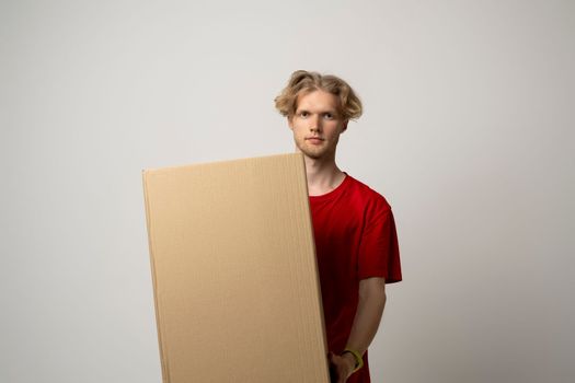 Young delivery man, courier in red cap and t-shirt standing with big parcel post box isolated over white background