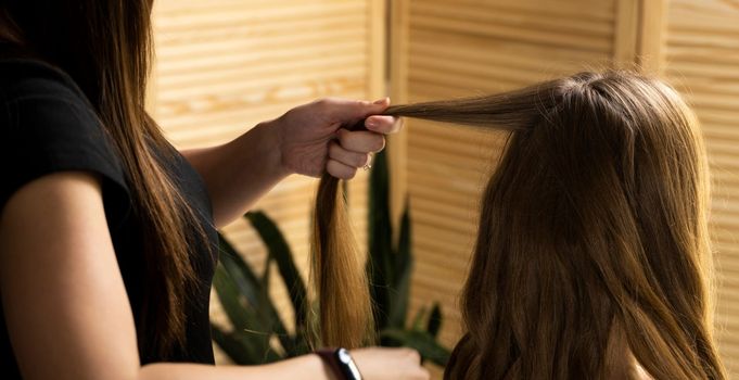 Hair stylist prepares woman makes curls hairstyle with curling iron in a beauty salon. Long light brown natural hair