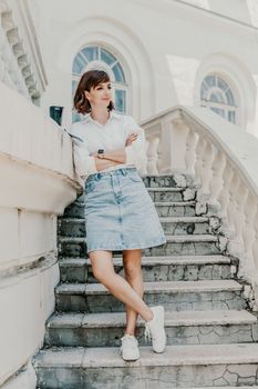 Woman building city. A business woman in a white shirt and denim skirt stands leaning against the wall on the steps of an ancient building in the city.