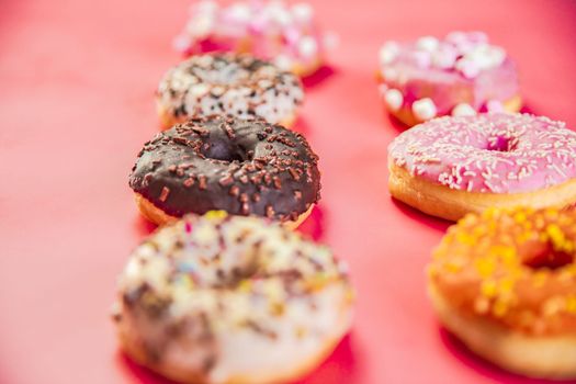Doughnuts with multicolored glaze laid out in two rows on trendy pink background. Doughnuts are traditional sweet pastries. Copy space for text. top view