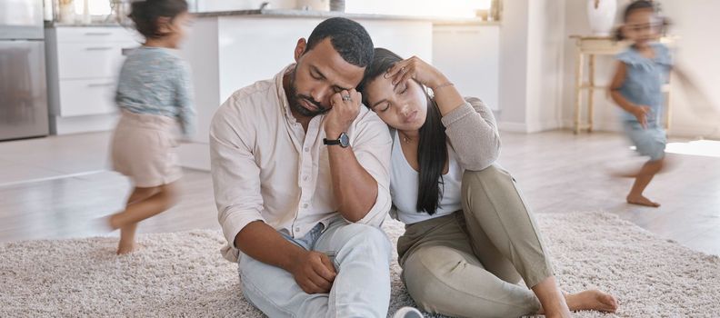 A young mixed race couple looking stressed at home while their kids play around them, Hispanic mother and father lacking energy as their kids play in the lounge at home.