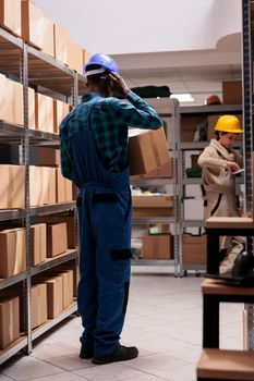 Delivery service worker holding cardboard box, preparing parcel for transportation in storage. Shipping business company warehouse operative wearing protective unifrom carrying carton