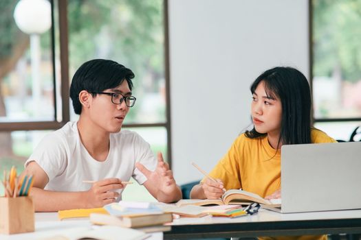 Young asian university students are studying for an exam. There are tutor books with friends. They are classmates that try to help each other. They have been tutoring for many hours in the campus.