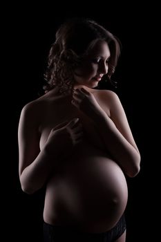 Pretty topless pregnant brunette isolated on black background