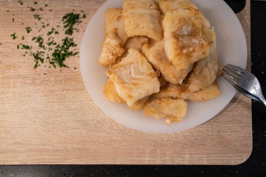 Pieces of fried hake loins over white plate and wooden cutting board. Preparing roman hake , Spanish recipe.