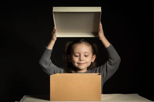 A little girl opens a long-awaited parcel with a gift, copy space on cardboard box.