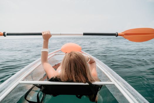 Woman in kayak back view. Happy young woman with long hair floating in transparent kayak on the crystal clear sea. Summer holiday vacation and cheerful female people having fun on the boat.