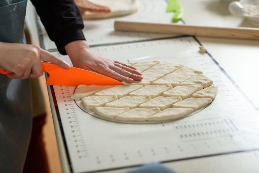 Side view of cutting dough with a plastic knife on a silicone baking mat.
