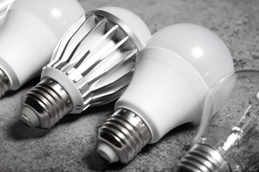 Incandescent lamp and various LED lamps with e27 base on gray background.