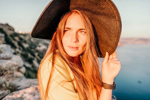 Portrait of happy young woman wearing summer black hat with large brim at beach on sunset. Closeup face of attractive girl with black straw hat. Happy young woman smiling and looking at camera at sea