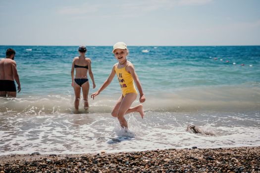 Cute little girl running along the seashore against a clear blue sea and rejoices in the rays of the summer sun. Beautiful girl in yellow swimsuit running and having fun on tropical beach