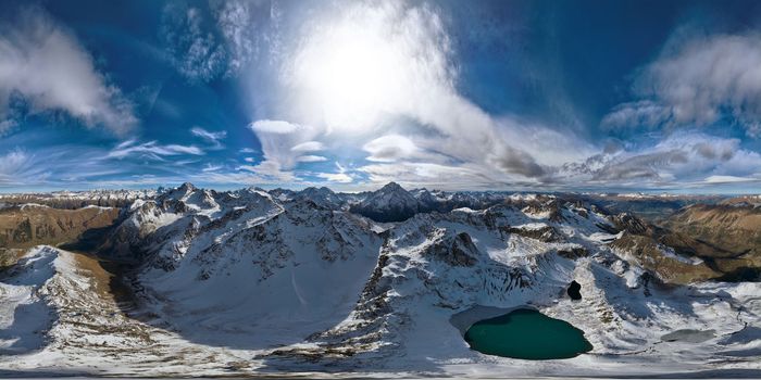 panorama of mountain snow-covered range with turquoise lake, sunny day with clouds.