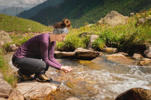 A woman tourist takes water in the river after a walk. Happy girl smiling while enjoying summer holidays outdoors in the mountains.