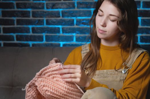 Portrait of a smiling blonde designer knitting clothes and accessories using yarn and crochet. Happy creative woman posing at home in comfortable interior, enjoying creativity or hobby.