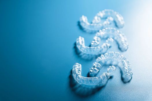 background for dental clinic or orthodontics. invisible plastic new braces lie in a row on a blue background, studio shot with shadows.