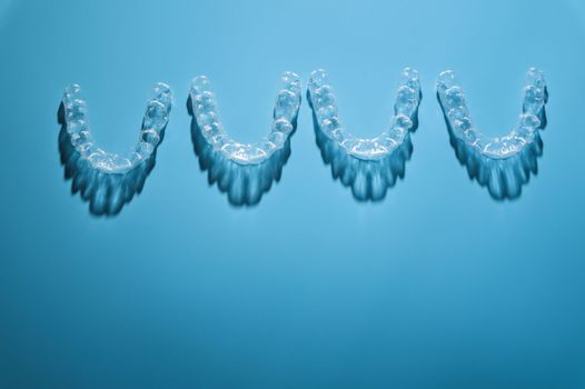 background for dental clinic or orthodontics. invisible plastic new braces lie in a row on a blue background, studio shot with shadows.