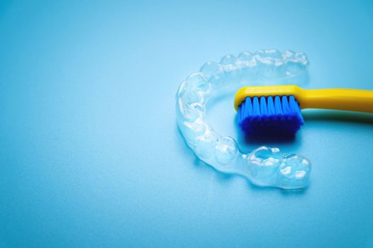 a bright toothbrush in yellow with plastic new braces lies on a blue background, no people.