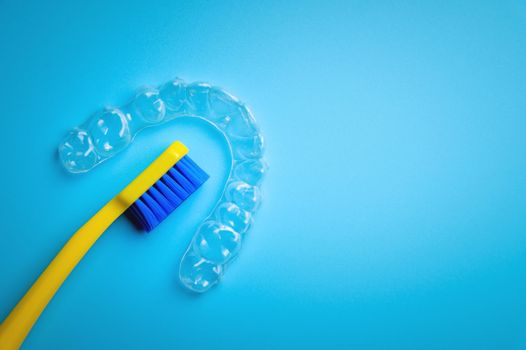 a bright toothbrush in yellow with plastic new braces lies on a blue background, no people.