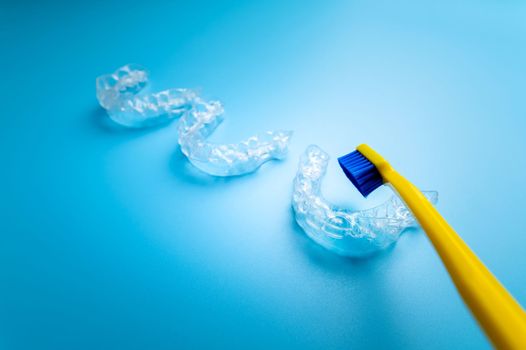 transparent aligners on a blue background with a bright yellow toothbrush, dental theme.