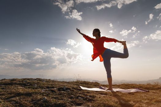 yoga warrior pose of young caucasian woman practicing at sunset in the mountains in the grass. Zen health and wellness concept.