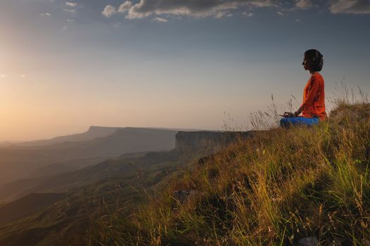 meditating woman sitting in lotus position near a cliff at sunset overlooking the mountains, practice in yoga, peace of mind.