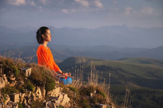 meditating woman with closed eyes in bright clothes in the mountains, sportswear advertising banner.